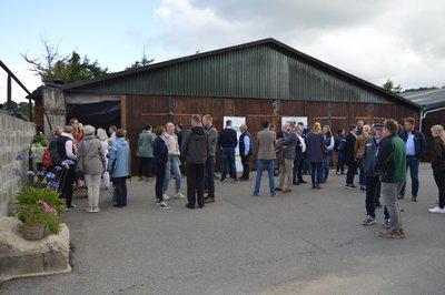 Eine Gruppe von Menschen steht vor einer Halle auf einem Landwirtschaftlichen Betrieb.