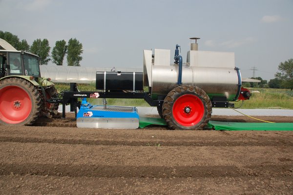 Ein Gerät zur thermischen Bodenbehandlung wird im Feld eingesetzt und von einem Trecker gezogen.