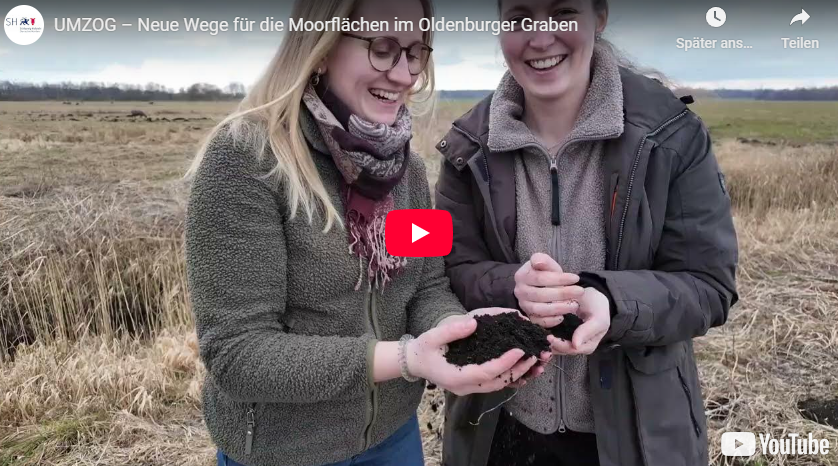 Zwei Personen stehen auf einem Moorfeld und halten gemeinsam ein Stück Moorboden in den Händen, Screenshot aus einem YouTube-Video zum Thema Moorrenaturierung